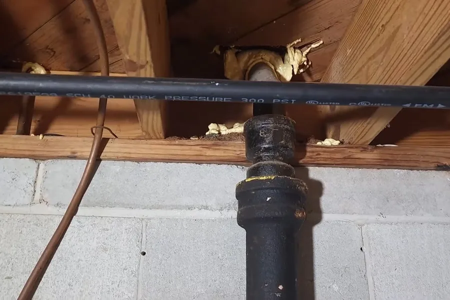 Black cast iron drain pipe in floor joists during a plumbing service call in Phoenix, AZ