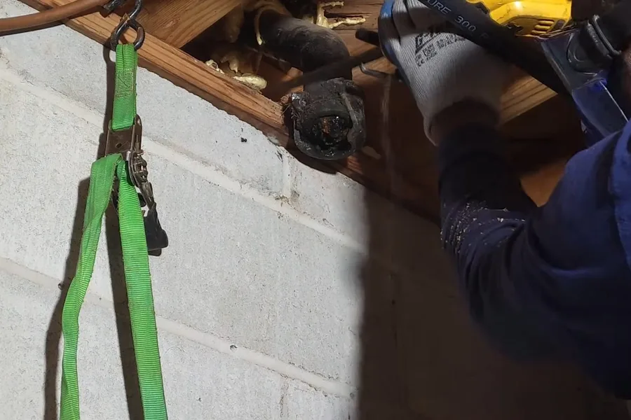 Plumber cutting overhead drain pipe in a basement during a plumbing service call in Rio Verde, AZ