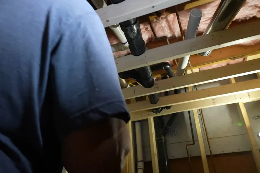Plumber working under open bathroom framing during a plumbing service call in Fountain Park Area, Fountain Hills, AZ